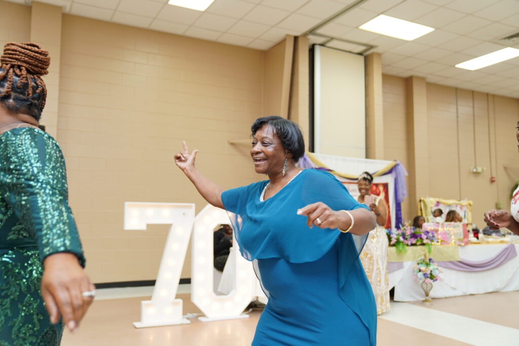 Lady in a blue dress dancing at birthday party with smile on her face