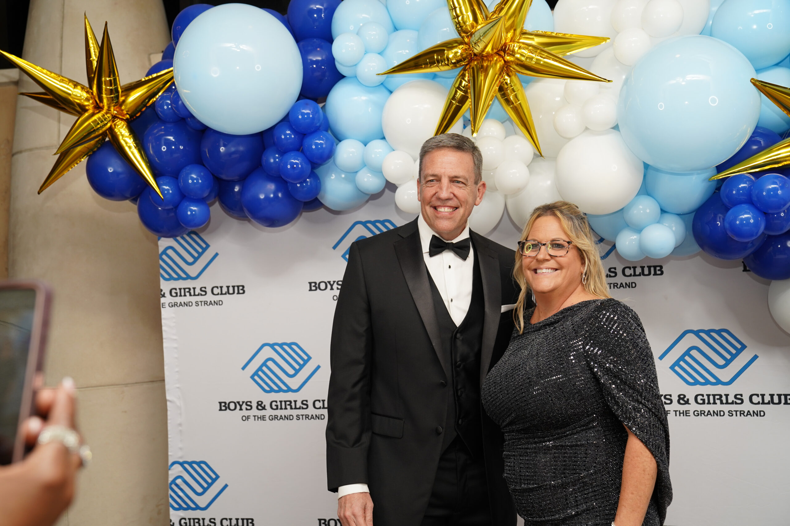 Ed Piotrowski smiling alongside the Champion of Youth honoree at the Myrtle Beach Boys and Girls Club of the Grand Strand event, standing in front of a colorful backdrop featuring the Boys and Girls Club logo, celebrating youth achievements and community impact.