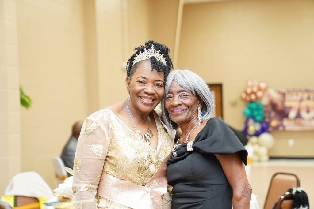 Elizabeth Hemingway Bowen poses alongside a woman in a black dress, both smiling warmly at the camera during her 70th birthday celebration.